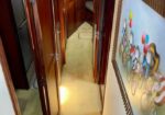 Narrow wood-paneled hallway aboard a boat with open doors and built-in cabinets, carpeted floor, leading to a lit rear area; wall art on the right.