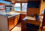 Wood-paneled yacht galley with a microwave, sink, and storage cabinets; marina visible through the windows.