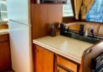 Compact boat galley with a white refrigerator, wood cabinets, beige countertop, sink, and a wall-mounted TV above.