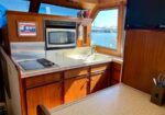 Compact boat galley with wood cabinets, stainless steel stove and microwave, and a white sink overlooking blue water through windows.