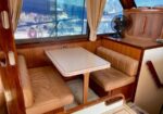 Boat cabin dining nook with beige leather benches, a small rectangular table, and wood paneling by a window.