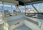 Boat cockpit with white cushioned seating and clear view of marina through windows; 'LIFE JACKETS' labeled storage beneath seats.