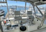Cockpit of a white yacht with a steering wheel, helm instruments, and two captain chairs at a marina.