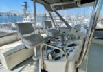 Helm station of a luxury motor yacht with a chrome steering wheel, gauges, and white seating, overlooking a marina.