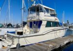 White motor yacht with blue trim docked at a wooden marina pier on a clear day.