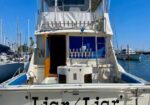Rear view of a white motor yacht named 'Liar Liar' with Long Beach, CA on the stern, docked at a marina under a blue sky.