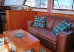 Leather sofa with teal geometric cushions in a wooden boat cabin, coffee table and window view of the marina