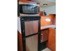 Compact galley with a stainless steel under-counter fridge/freezer, a microwave on top, and wooden cabinets along a small kitchen nook.
