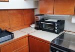 Countertop with a black toaster oven, coffee maker, and dish rack on a beige surface in a compact wooden-cabinet kitchen.