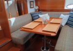 Wooden boat dining table set with four placemats and a vase of white flowers, surrounded by plaid upholstered benches.