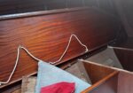 Close-up of a glossy wooden surface with a grey cushion and a red fabric patch, a white rope resting on it in a dim interior.
