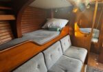 Cozy sailboat cabin with varnished wood walls, a long gray upholstered bench, and a patterned pillow resting on the cushion.