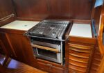 Stainless steel gas stove with grill built into a wood-paneled kitchen area, blue towel hanging on the right.