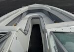 Bow seating area of a white motorboat with light gray cushions and a center walkway, photographed from the passenger side near the windshield edge