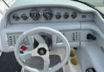 Boat helm with a gray dashboard, white steering wheel, and multiple round gauges plus switch panels on the console.
