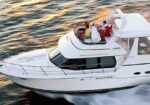 White luxury motor yacht cruising on open water with two people on the upper deck.