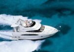 White luxury motor yacht speeding on clear blue ocean with two people on the deck.