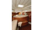 Cozy yacht cabin featuring a circular bed with striped bedding and pillows, wood cabinetry, and a skylight.