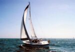 Sailboat with white sails gliding on blue sea under a clear sky with a few clouds.