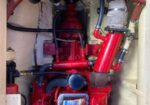 Red marine engine in a compact engine room, with large red hoses, metal clamps, and wiring visible.