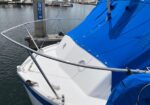 White motorboat at a marina with a bright blue canvas covering its deck and stainless railings along the bow.