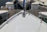 Bow of a sailboat at a marina, showing stainless guard rails, anchor roller, and surrounding docked boats.