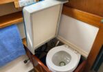 Open cabinet reveals a portable marine toilet in a small head, with a blue towel nearby.