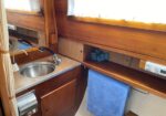 Compact boat galley with a stainless sink, wooden cabinets, and a blue towel hanging below the counter.