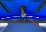 Close-up of a metal pulley winch mounted under a blue canopy, with an orange rope threaded through it and secured.
