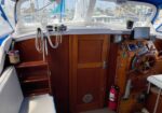 Boat cockpit with wooden helm, gauges, and seating; marina with other boats visible through the windshield (yacht dock).