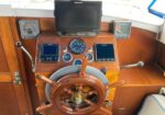 Wooden boat helm with polished steering wheel, compass, and multiple navigation displays on a varnished dashboard.