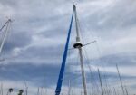 Sailboat mast with a blue sail cover in a marina, other masts in the background under a cloudy sky.