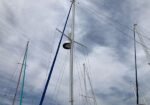 Cluster of sailboat masts and rigging rising into a cloudy blue sky at a marina.