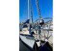 Sailboat moored at a marina, view of the stern, deck, and rigging against a bright blue sky.