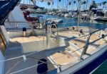 Sailboat cockpit with a steering wheel, wooden deck, and stainless rails at a marina with other boats in the background