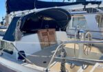 Sailboat in a marina with a blue canopy, coiled lines, and a wooden cabinet leaning against the cabin in the cockpit area.
