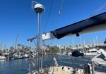 Sailboats docked in a sunny marina, viewed from a deck with rigging and a folded sail in the foreground.