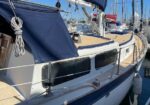 Sailing yacht docked at a marina with a blue cockpit cover and wooden deck railing details visible