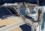 Sailing boat deck with lines, winches, and rigging, marina visible in the background.