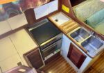 Compact boat galley with stove/oven, cutting board, and double sink along wooden counters and cabinets.