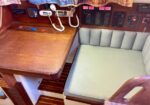 Wooden navigation desk with mounted radios and a coiled cord phone beside a light-blue cushioned bench on a sailboat interior.
