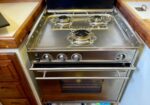 Gas stove with three burners and a front oven, installed in a wooden kitchen cabinet.