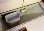 Open chest freezer showing a white plastic tub/basket inside and a small control box mounted on the inner wall.