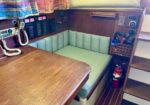 Cozy boat cabin corner with a wooden table, light-green bench seating, and navigation panels on the wall. A fire extinguisher is nearby.
