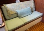 Light green cushioned bench seat along a wooden cabin wall, with a woven throw blanket and a blue decorative pillow.