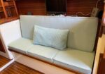 Light blue cushioned bench with a matching lumbar pillow in a wood-paneled boat cabin, TV and cables on the wall behind.