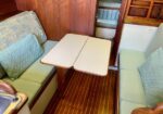 Boat cabin dining area: two green upholstered benches opposite each other with a drop-leaf table, wood walls, and a sink to the left.