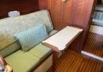 Boat cabin with green cushioned seating, pale pillows, and a fold-out cream dining table attached to the wall.
