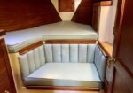 Light blue cushioned seating area around a small boat cabin with a V-berth bed and wooden paneling on the walls and cabinets