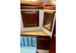 Wooden wall cabinet and mirrored panel above a light wood countertop in a compact boat cabin, with a blue cushioned bench below.